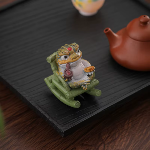 Tea pet rana dorata in resina su poltrona a dondolo