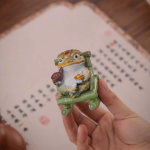 Tea pet rana dorata in resina su poltrona a dondolo